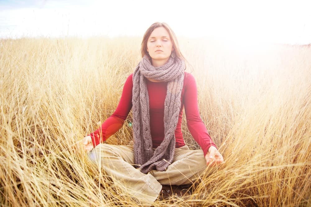 Woman meditating in a field of tall golden grass. Different ways to meditate