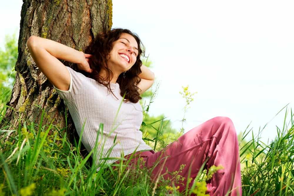 Woman relaxing against a tree, experiencing positive emotions