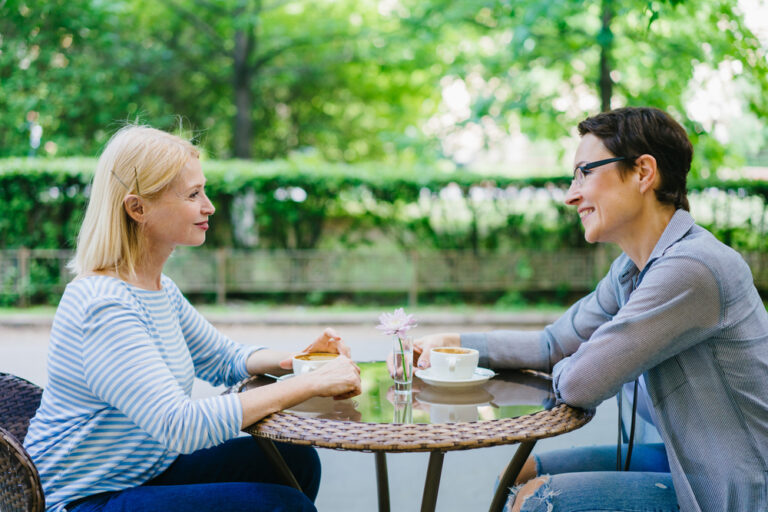 Mature lady talking to friend in open air cafe. smiling and supporting each other