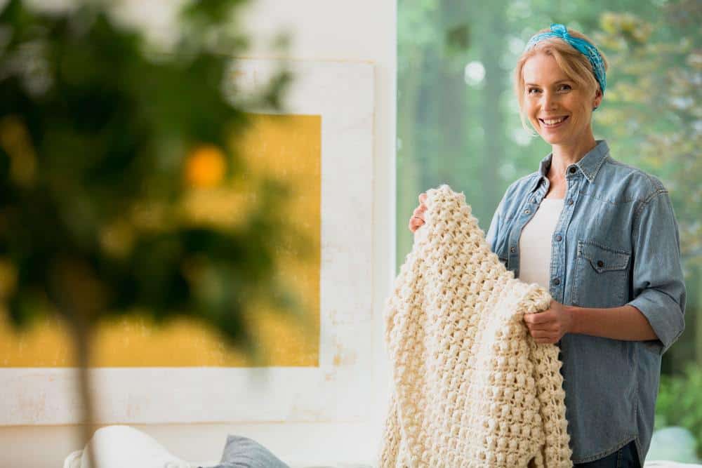 Smiling woman holding a chunky knit blanket. Housework as life purpose